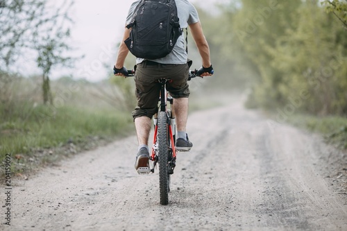 Man riding a bicycle at countryside road. Cyclist with backpack in motion, view from the back. Sports, tourism and activity concept