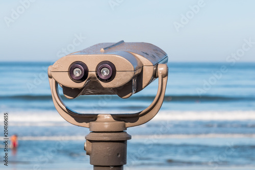 Sightseeing binoculars overlooking the ocean, with a blurred person in the water.