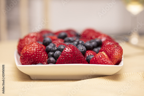 Plate filled with red strawberries and blueberries on a table with linen photo