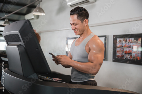 Asian muscular man on treadmill holding smartphone