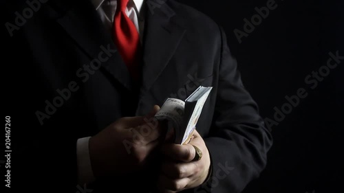 Photo of a rich businessman in black siut with red tie holding and counting money pack.