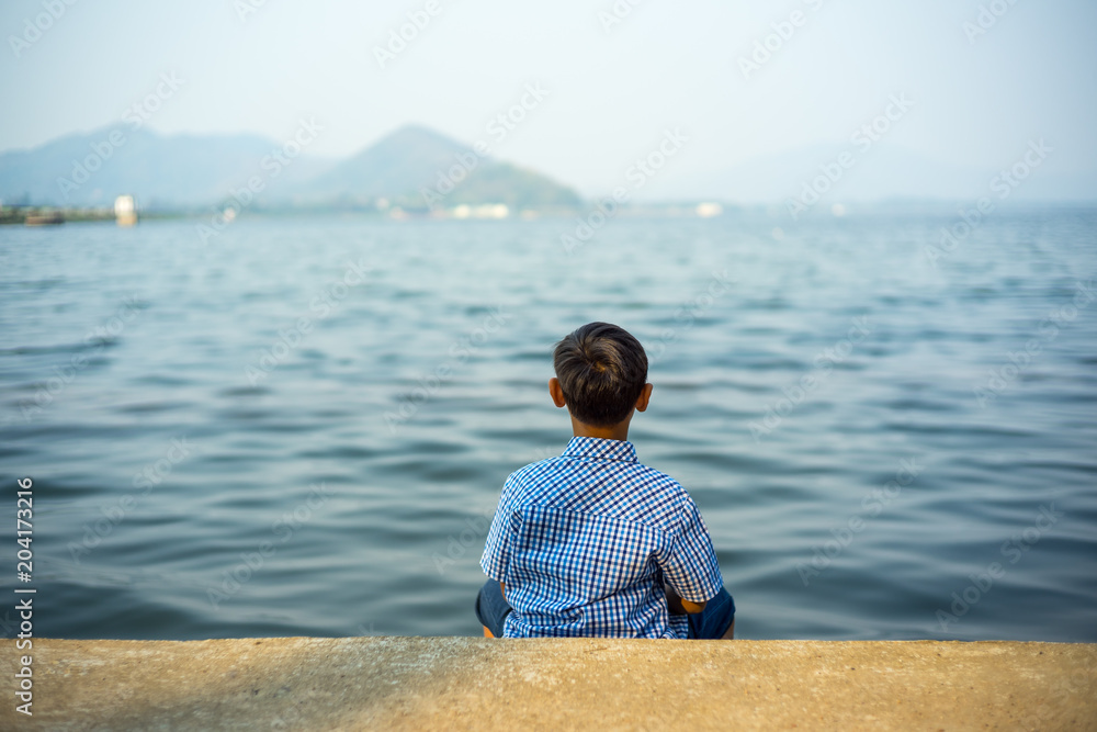The boy sitting on the waterside  overlooking view at Bang Phra reservoir chonburi thailand.