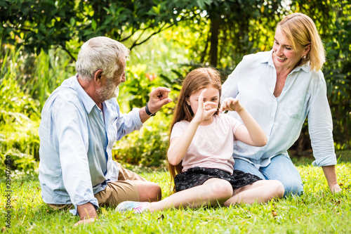 Happy family having fun together in the garden. Father, mother and daughter sitting on grass in a park. © ronnarong