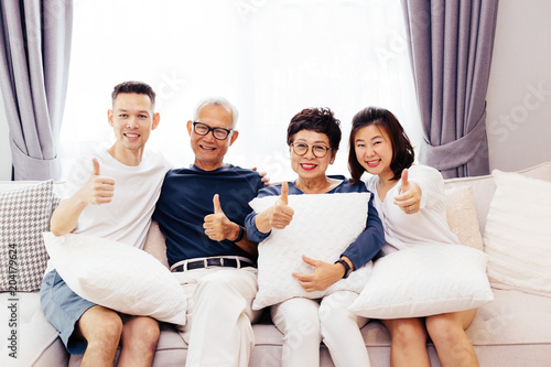 Asian family with adult children and senior parents giving thumbs up and relaxing on a sofa at home together. Happy family time together © twinsterphoto
