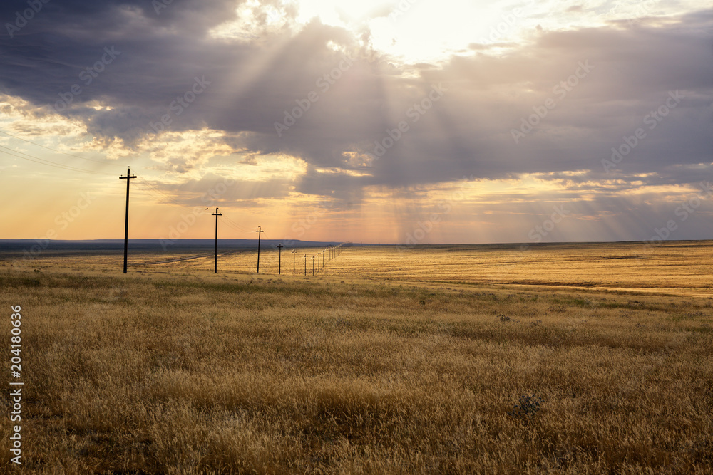 Morning steppe landscape with sun rays over clouds and power-transmission poles