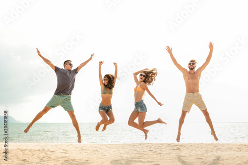 Happy young energetic group of friends jumping at the beach in summer