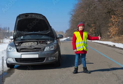Boy in a waistcoat on the road near a car with a prolate hand, asks a technical help.