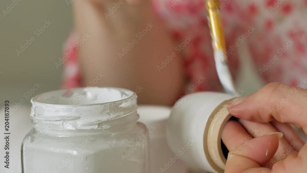 A woman paints a wooden doll with colored paints in her home studio, Matryoshka painting, Close-up A woman paints a wooden doll with colored paints in her home studio, Matryoshka painting, Close-up