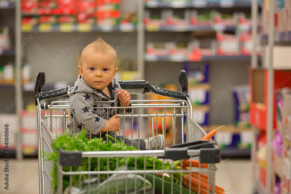 Toddler baby boy sitting in a shopping cart in grocery store smiling and eating bread Stock Foto Adobe Stock