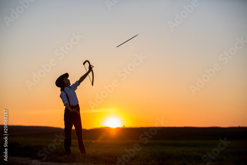 Silhouette of child playing with bow and arrows, archery shoots a bow at the target.