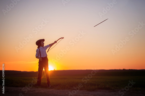 Silhouette of child playing with bow and arrows, archery shoots a bow at the target.