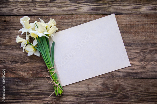 Bouquet of white with yellow daffodils and sheet of paper for writing on wooden background