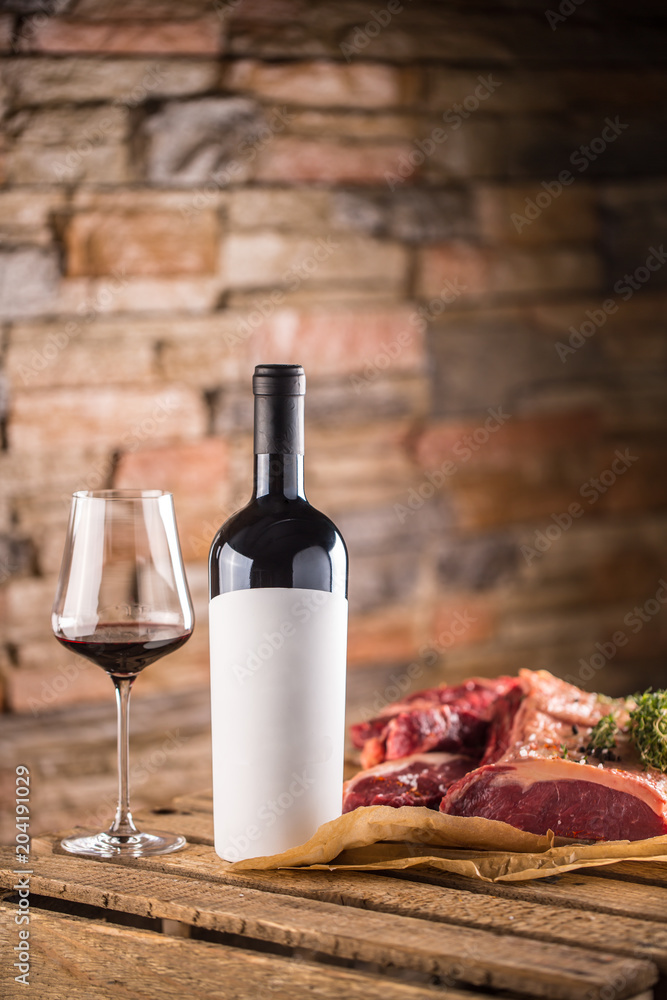 Naklejka premium Cup and a bottle of red wine and raw beef steak on wooden table