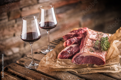 Two cups with red wine and raw beef steak on wooden table