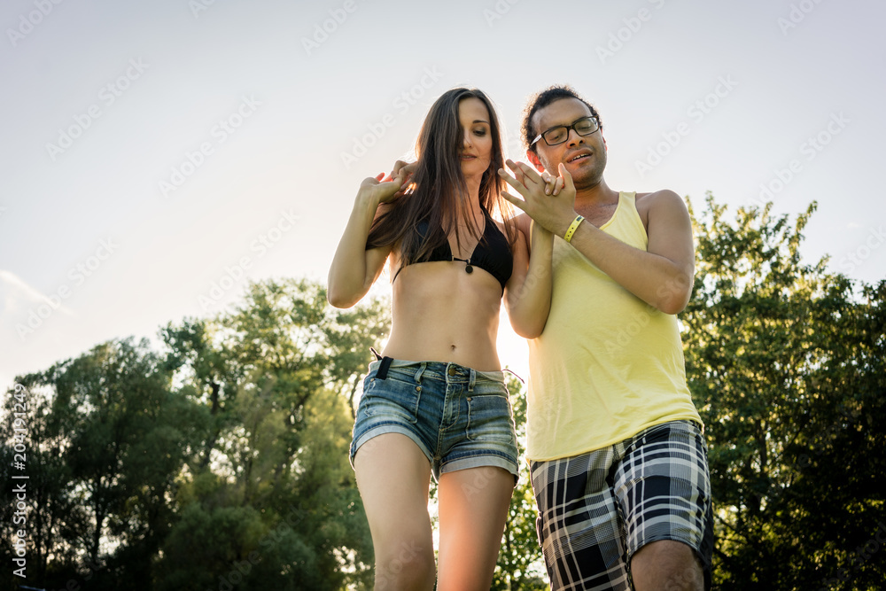 Man turning woman dancing in the grass in summer park