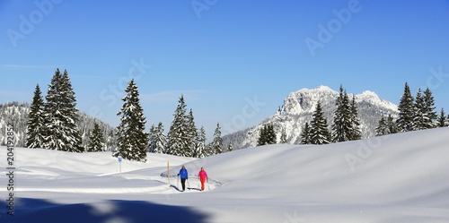 Two hikers walk through snow-covered mountain scenery, premium winter hiking trail, Hemmersuppenalm, Reit im Winkl, Chiemgau, Oberbayern, Bavaria, Germany. photo
