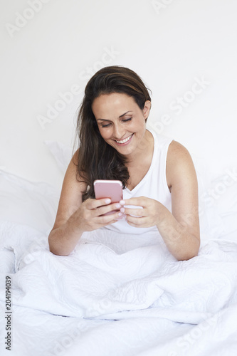 Brunette in phone in bed, smiling