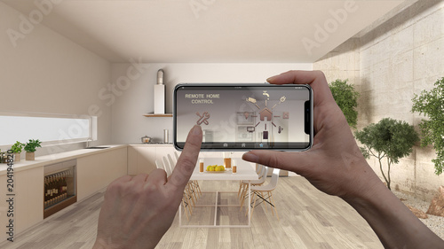 Remote home control system on a digital smart phone tablet. Device with app icons. Interior of minimalist white kitchen in the background, architecture design. photo