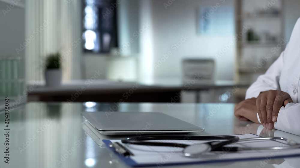 Doctor sitting at table with closed laptop, starting new workday in clinic Doctor sitting at table with closed laptop, starting new workday in clinic