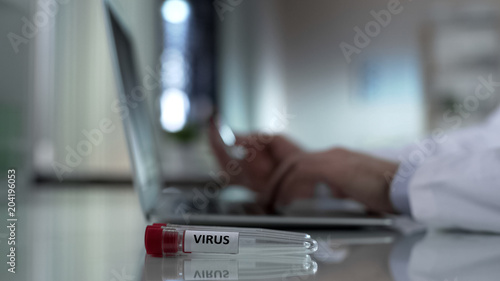 Lab worker typing on computer, virus sample in test tube, epidemic prevention
