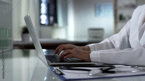 Physician typing on laptop, patients medical record, healthcare technology