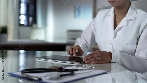 Female doctor scrolling tablet screen, checking patients test results, clinic