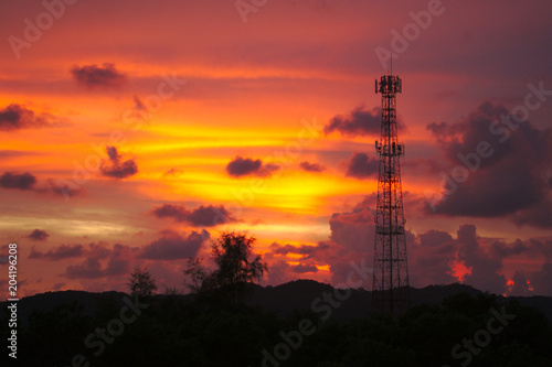 tall mobile cell phone tower on the high hill in Chantaburi, Thailand sending signal to connect people around the world in the evening when sunset with orange red sky and clouds