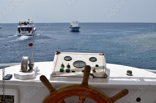 Ship with wooden steering wheel and navigation console at the helm of a yacht or motor boat, follows other yachts on the high seas. nobody in the frame.