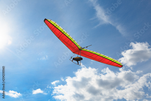 Fotografie The hang glider on a red hang-glider is flying in a blue sky