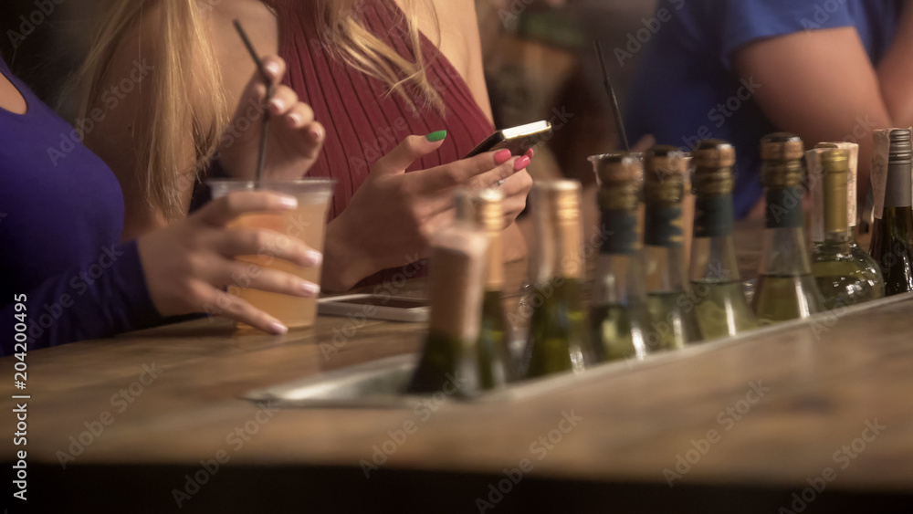 Women hanging out, having drink at bar counter, chatting online on smartphones