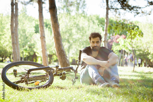 Cyclist resting on the ground in the grass next to his bicycle