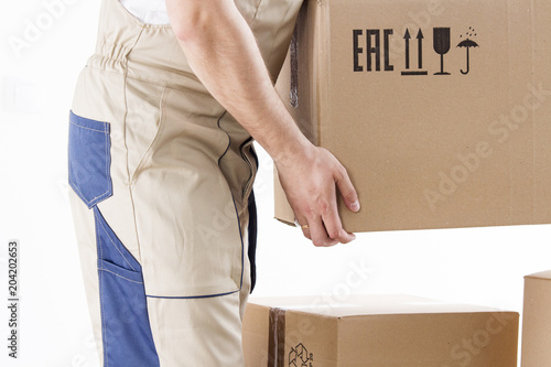 Close-up of hand of loader holding cardboard box isolated on white background. Loader picks up box. Mover holds cardboard box closeup. Relocation service man.