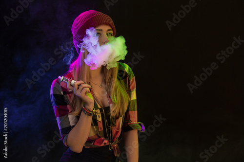 Vaping girl. Young hipster woman vape e-cig on black background. Hip-hop style. Studio shot
