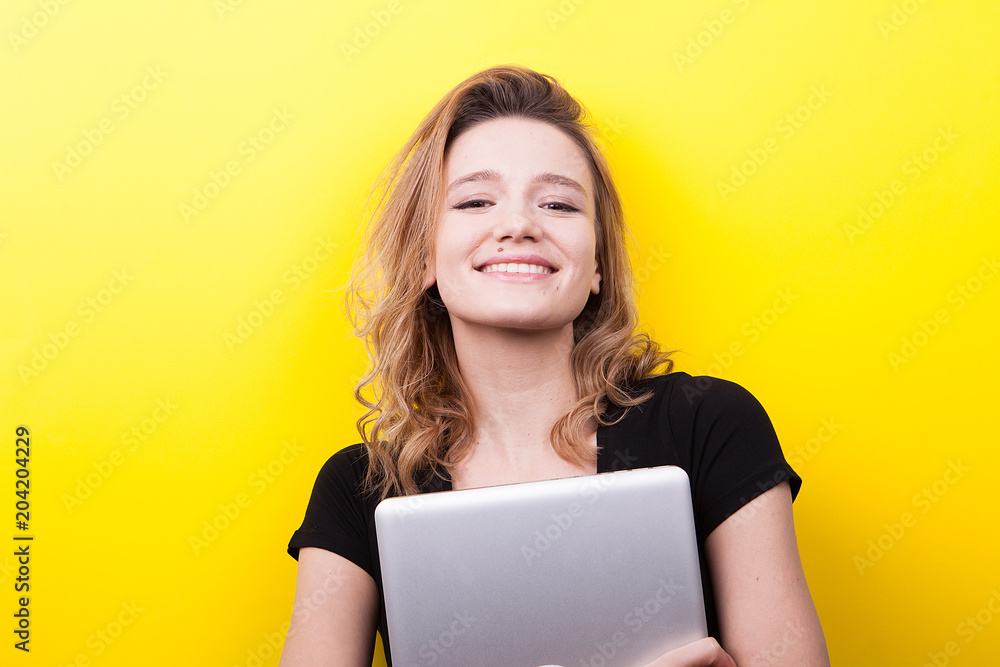 Beautiful student woman holds a laptop in hands on yellow background in studio photo Beautiful student woman holds a laptop in hands on yellow background in studio photo