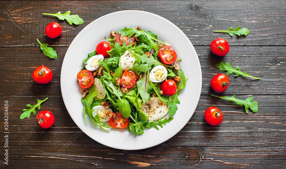 Fresh salad with tomatoes, mixed greens ,nuts, eggs, on wooden background . Healthy food.