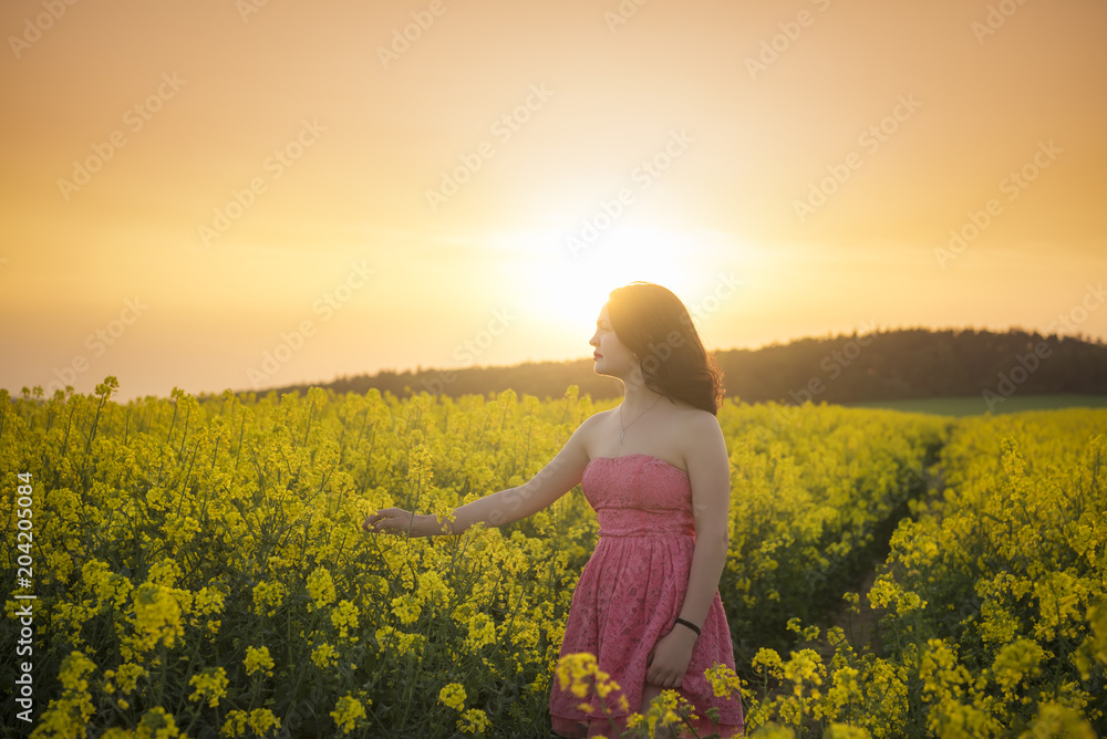 Fototapeta premium Woman in a rapeseed field at sunset