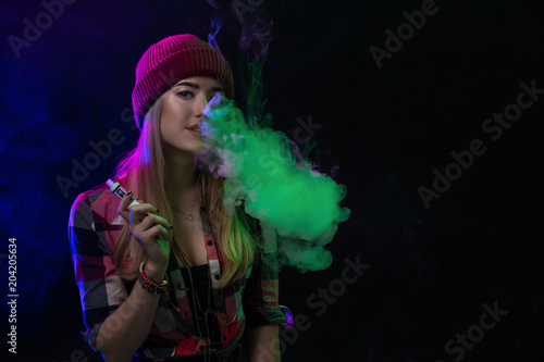 Vaping girl. Young hipster woman vape e-cig on black background. Hip-hop style. Studio shot