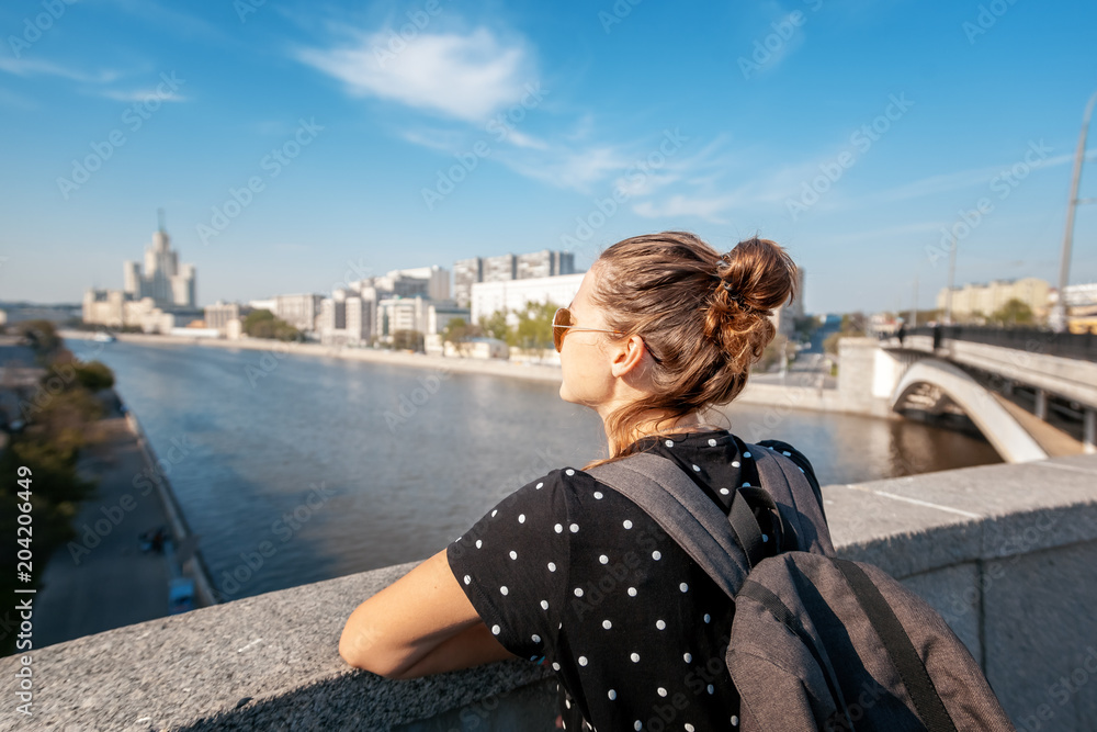 A young tourist woman admires the view of the center of Moscow and the river on a summer sunny day, a travel to Russia