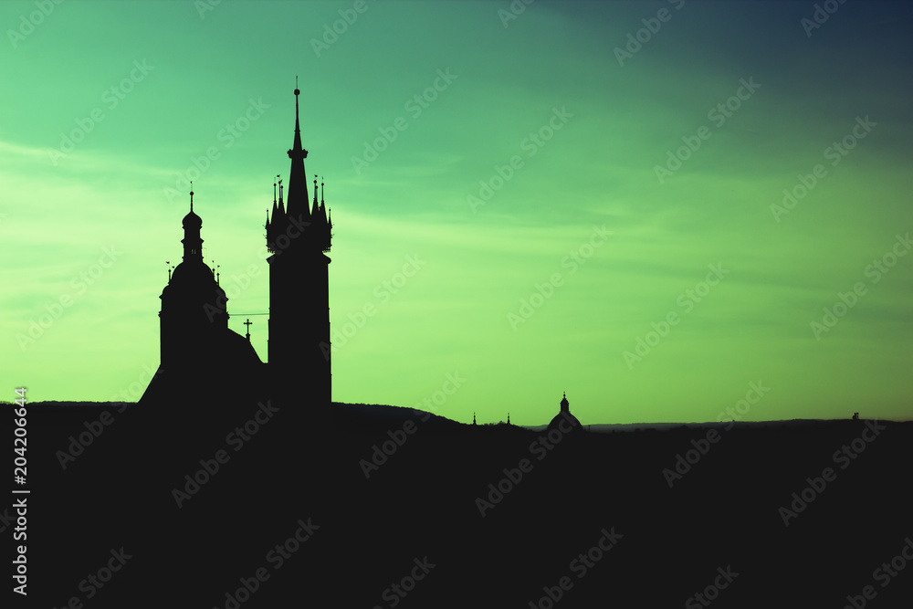 Black silhouette St. Mary Basilica in Krakow and panorama of the city center against a background of sunset and a fantastic green sky