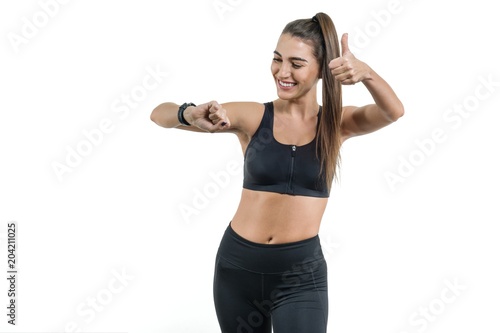 Portrait of smiling young fitness female looking at wrist watch, isolated. Woman happy, gesture showing thumbs up