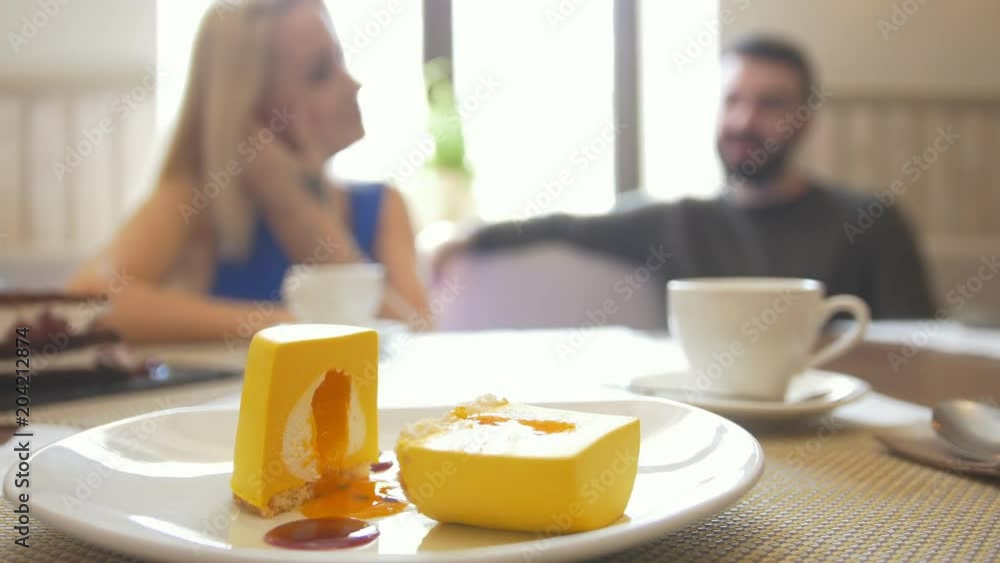 Sweet sliced dessert on plate in front of happy couple talking at the cafe Sweet sliced dessert on plate in front of happy couple talking at the cafe