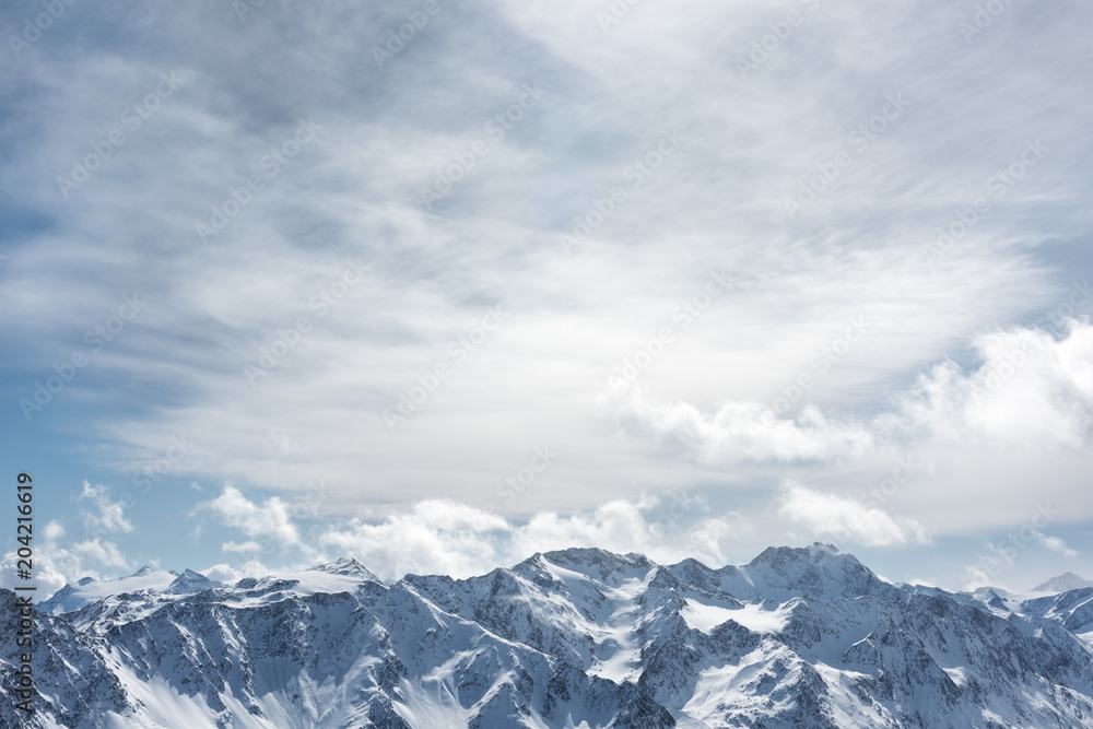 Winter Alpine landscape. The snowy peaks of the high mountains against cloudy sky
