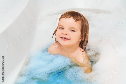 Funny child playing with water and foam in a bathroom. child bathes.