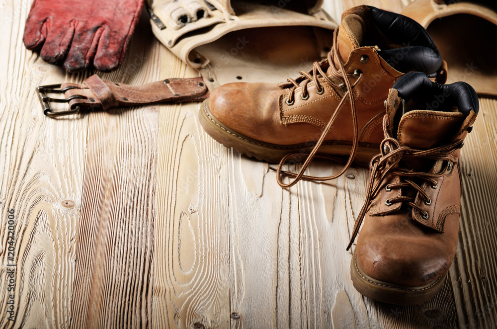 Yellow leather used work boots with tool belt and protective gloves on wooden background closeup. Place for text
