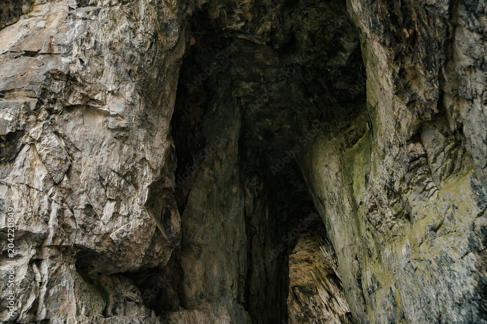 Beautiful cave. View from inside dark dungeon. Textured walls of cave. Background image of underground tunnel. Dampness inside cave. Light at end of tunnel.