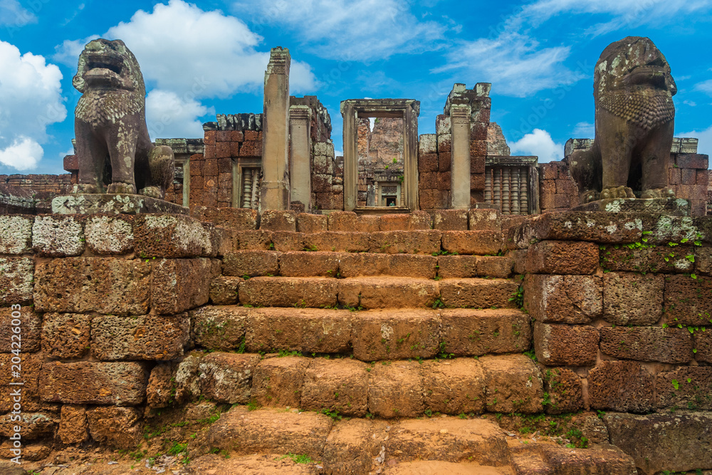 Front view of the terraced landing of the East Mebon temple in Cambodia. The staircase, guarded by two lion statues, is leading to the entry tower of the temple, dedicated to the Hindu god Shiva.