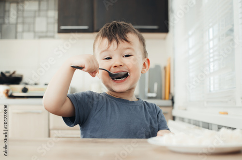 The little boy in the kitchen eagerly eating rice with a spoon independently photo