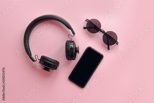 stylish black sunglasses,smartphone and headphones on pink background, flat lay. modern hipster image. black items on pink paper. instagram blogging. space for text. summer vacation