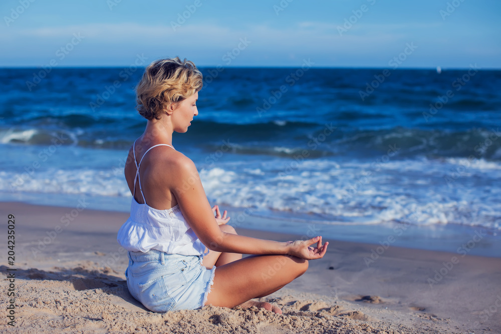 Young woman meditating on beach, pier in lotus position at sunrise Young woman meditating on beach, pier in lotus position at sunrise