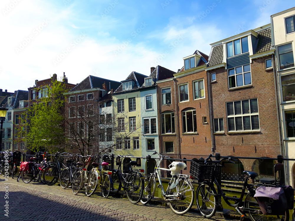 Bicycles against a fence along a Dutch canal with canal houses. Utrecht, The Netherlands, Europe.